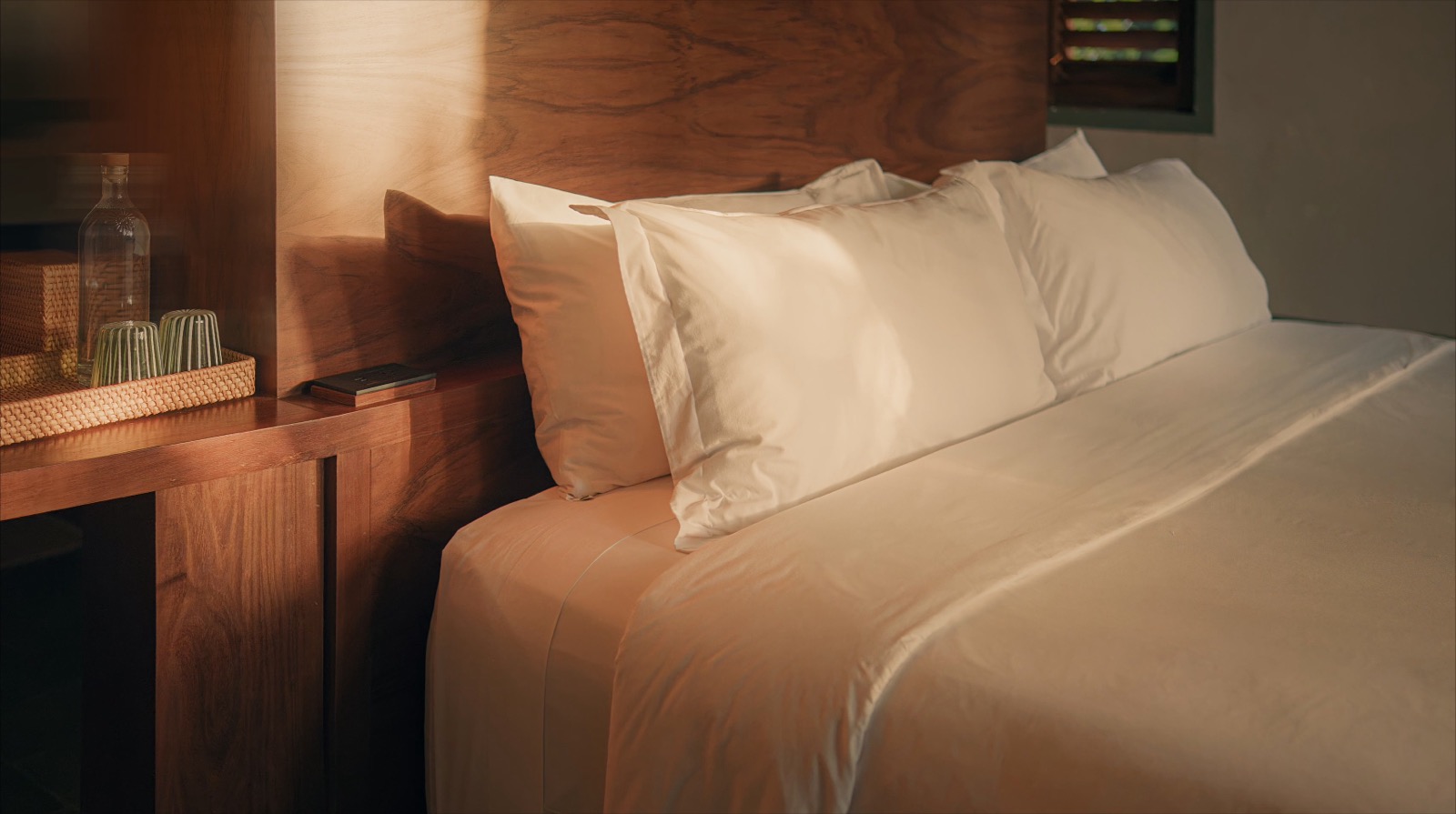 A bed dressed in white linen beneath a wooden headboard